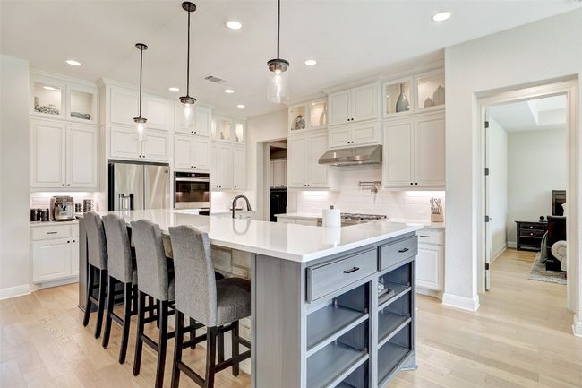 Kitchen featuring appliances with stainless steel finishes, under cabinet range hood, white cabinets, large island with sink | Image 9