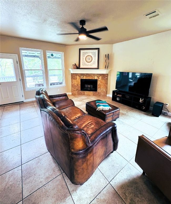 Living area featuring a ceiling fan, a premium fireplace, a textured ceiling, and tile patterned floors. | Image 6