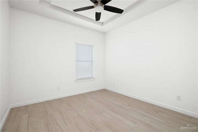 Empty room with a raised ceiling, wood finished floors, and a ceiling fan | Image 6
