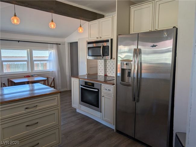 Kitchen featuring stainless steel appliances, hanging light fixtures, dark wood finished floors, and lofted ceiling with beams | Image 5