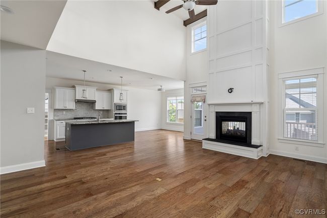 Unfurnished living room with high vaulted ceiling, ceiling fan, dark wood-type flooring, and a multi sided fireplace | Image 8