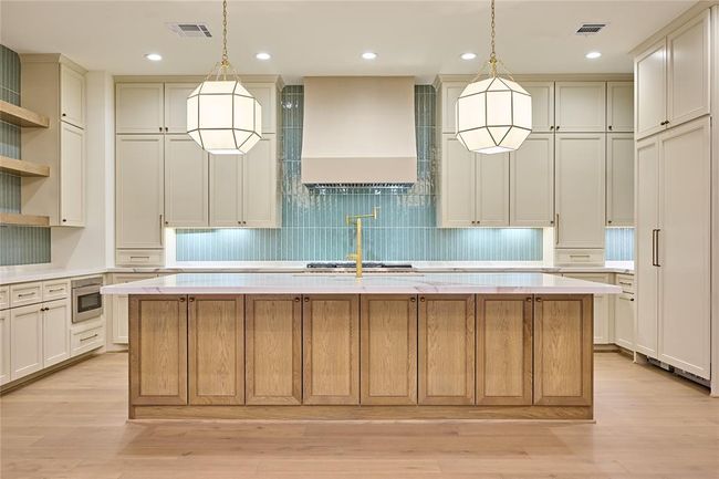 This kitchen features a spacious island with a wood finish, elegant pendant lighting, and ample cabinetry for storage. The design includes a modern backsplash, high-end appliances, and a bright, open layout. Perfect for cooking and entertaining. | Image 14