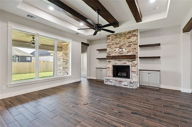 Unfurnished living room featuring ceiling fan, dark wood finished floors, baseboards, beam ceiling, and a fireplace | Image 9