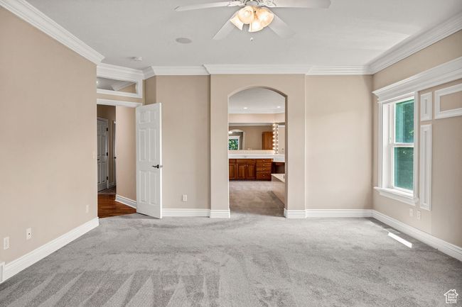 Carpeted spare room featuring arched walkways, crown molding, ceiling fan, baseboards, and a smoke detector | Image 15