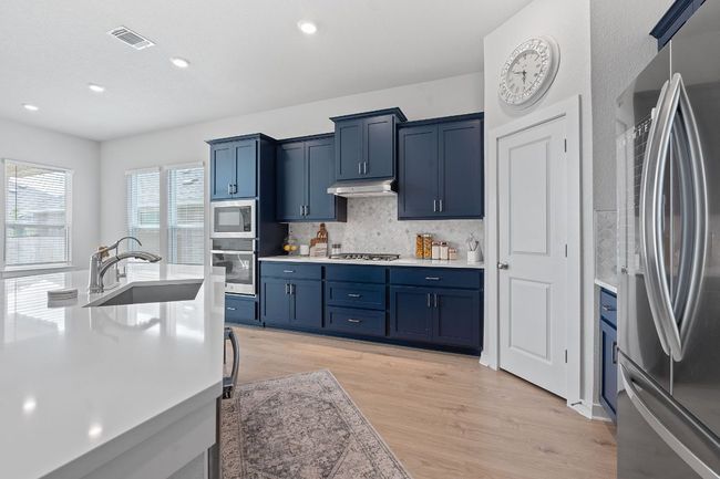 Kitchen with under cabinet range hood, stainless steel appliances, light countertops, blue cabinets, and a sink | Image 11