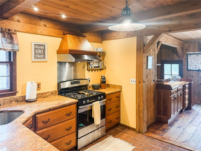 Kitchen featuring brick floor, wood walls, wood ceiling, beam ceiling, and gas stove | Image 13