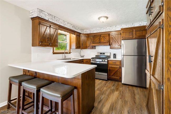 Kitchen featuring custom range hood, kitchen peninsula, stainless steel appliances, hardwood / wood-style flooring, and sink | Image 11