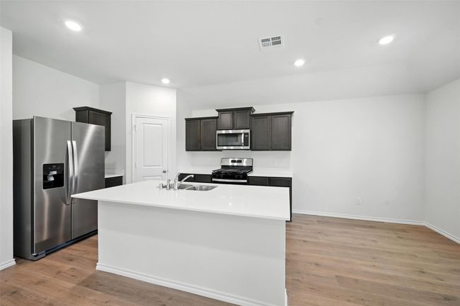 Kitchen featuring stainless steel appliances, light wood-style floors, light countertops, an island with sink, and recessed lighting | Image 5