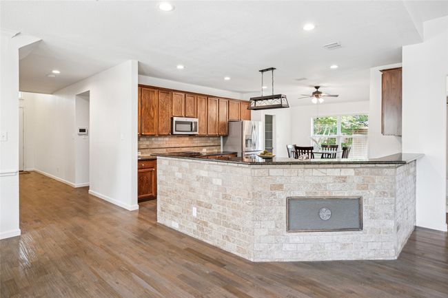 Kitchen featuring stainless steel appliances, dark countertops, a ceiling fan, dark wood-style floors, and brown cabinetry | Image 12