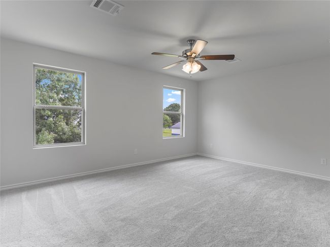 Spacious master bedroom with plush carpeting and a stylish ceiling fan for comfort and elegance. | Image 12
