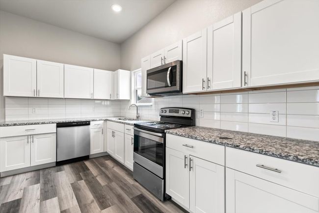 Kitchen with dark stone countertops, white cabinetry, stainless steel appliances, and dark wood-type flooring | Image 11