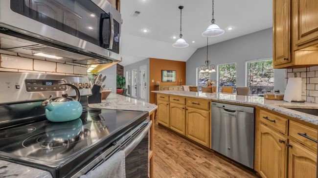 Kitchen with light stone countertops, a chandelier, light wood-style floors, and stainless steel appliances | Image 6