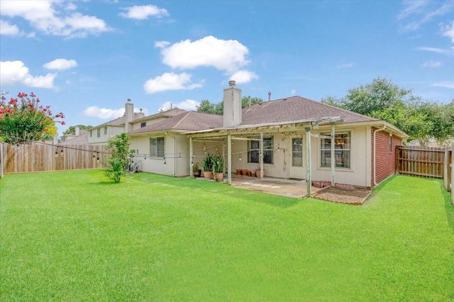 This photo showcases a charming backyard with a well-maintained lawn, a covered patio, and privacy fencing, perfect for relaxation and outdoor gatherings. | Image 28