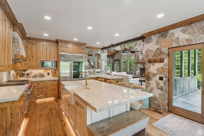 Kitchen with built in appliances, premium range hood, light wood-type flooring, a kitchen breakfast bar, and a stone fireplace | Image 9