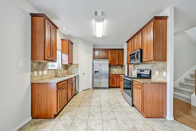 Kitchen with appliances with stainless steel finishes, light stone counters, decorative backsplash, and brown cabinetry | Image 5