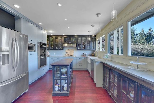 Kitchen with stainless steel appliances, under cabinet range hood, glass insert cabinets, decorative light fixtures, and dark wood-type flooring | Image 14