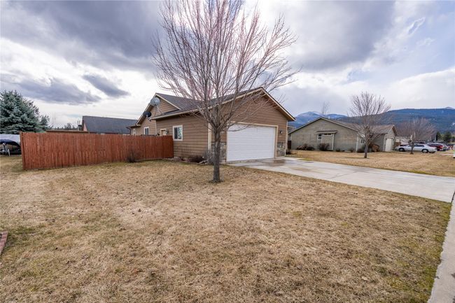 View of side of property with a yard, concrete driveway, an attached garage, and fence | Image 34