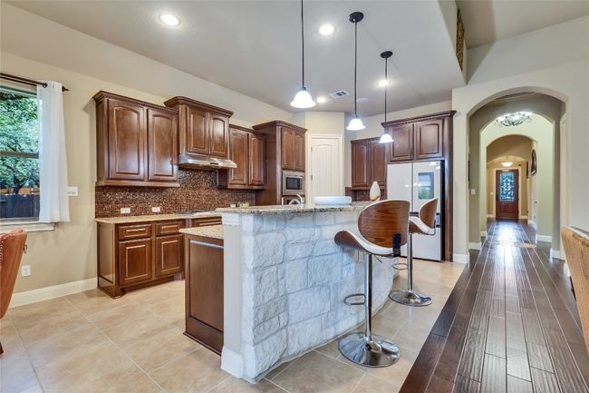 Gourmet kitchen featuring stainless steel appliances, under cabinet range hood, granite countertops, arched walkways, and decorative backsplash | Image 22