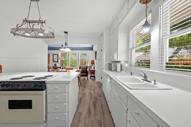 Kitchen featuring white appliances, white cabinets, light wood-style flooring, light countertops, and hanging light fixtures | Image 11