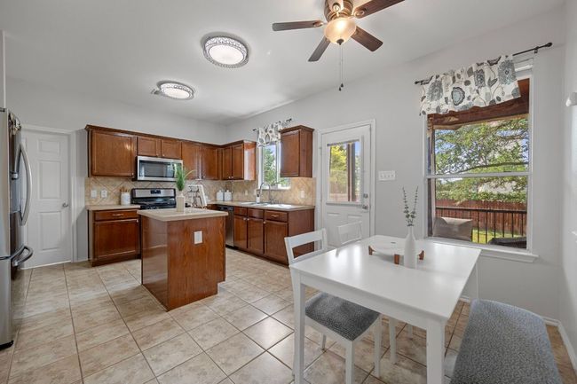 Kitchen featuring appliances with stainless steel finishes, a kitchen island with sink, tasteful backsplash, light countertops, and ceiling fan | Image 13