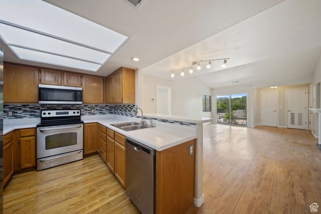 Kitchen featuring stainless steel appliances, light countertops, a peninsula, open floor plan, and light wood-style flooring | Image 7
