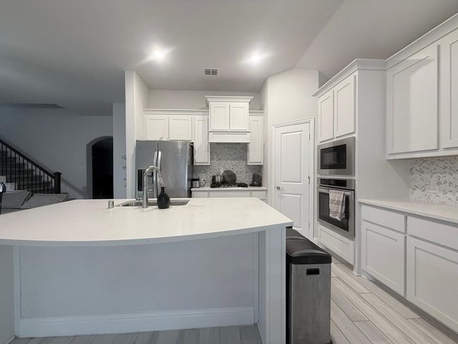 Kitchen with appliances with stainless steel finishes, backsplash, arched walkways, and white cabinets | Image 9