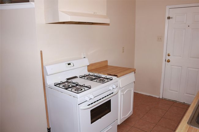 Kitchen with white range with gas stovetop, under cabinet range hood, white cabinetry, light tile patterned floors, and light countertops | Image 11