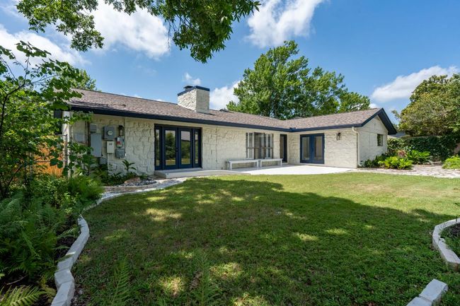 Back of property featuring french doors, a chimney, stone siding, a lawn, and a patio area | Image 29