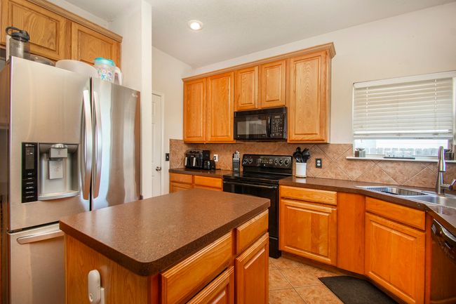 Kitchen with black appliances, dark countertops, decorative backsplash, a sink, and light tile patterned flooring | Image 7