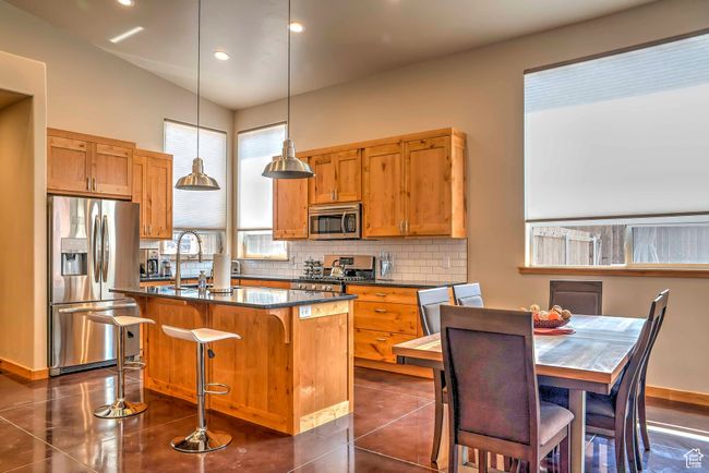 Kitchen featuring stainless steel appliances, dark countertops, a sink, tasteful backsplash, and an island with sink | Image 6