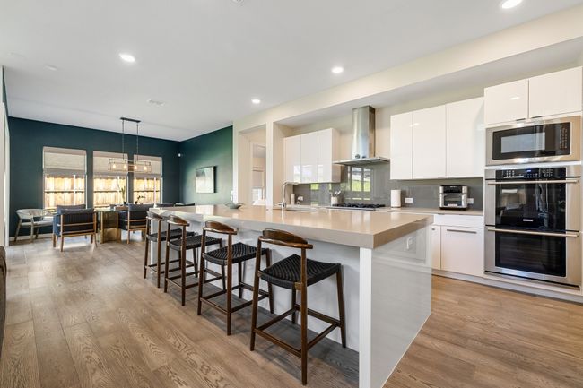 Kitchen featuring wall chimney range hood, stainless steel appliances, modern cabinets, hanging light fixtures, and light wood-style flooring | Image 10