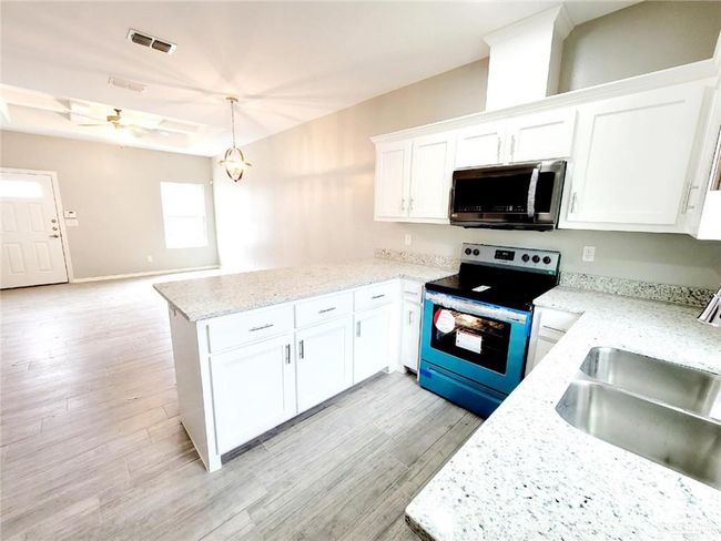 Kitchen with light wood finished floors, a peninsula, a sink, white cabinetry, and appliances with stainless steel finishes | Image 6