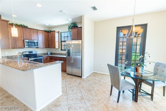 Kitchen featuring a notable chandelier, light stone countertops, visible vents, brown cabinetry, and stainless steel appliances | Image 12