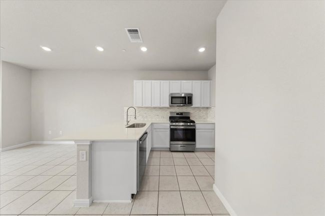 Kitchen with stainless steel appliances, a sink, light tile patterned floors, decorative backsplash, and recessed lighting | Image 9