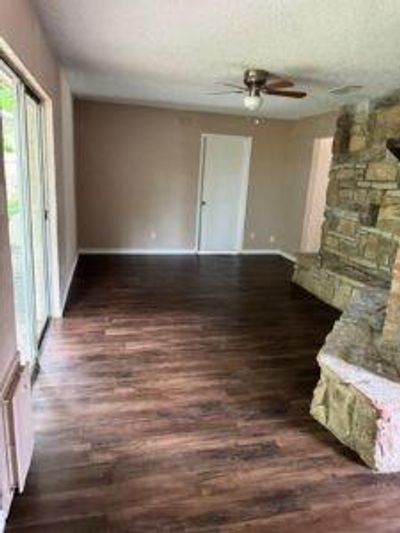 Unfurnished living room featuring dark wood-type flooring, ceiling fan, and a stone fireplace | Image 3