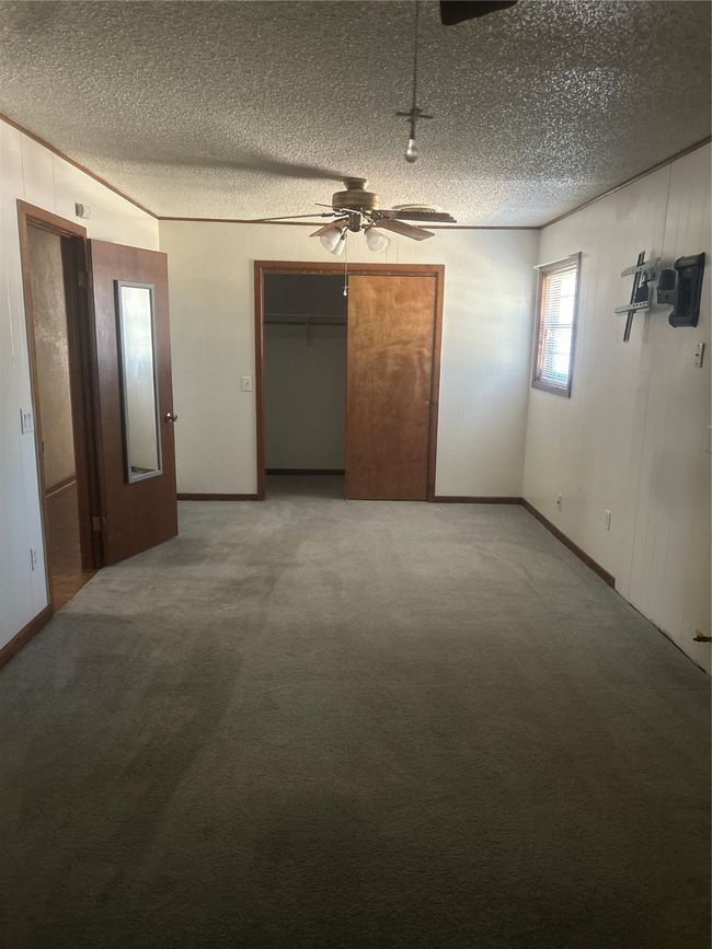 Carpeted empty room with a textured ceiling, ceiling fan, baseboards, and wooden walls | Image 9