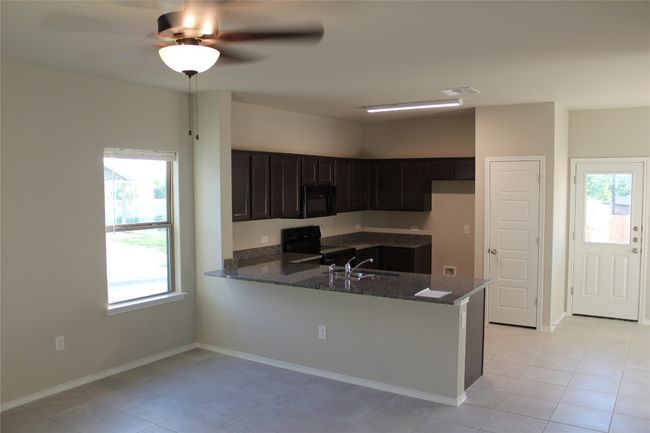 Kitchen featuring black appliances, dark stone counters, a peninsula, light tile patterned floors, and a sink | Image 4