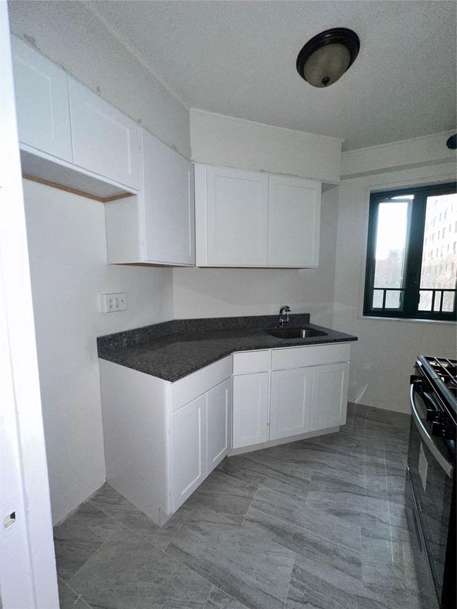 Kitchen with a sink, stove, dark countertops, and white cabinets | Image 8