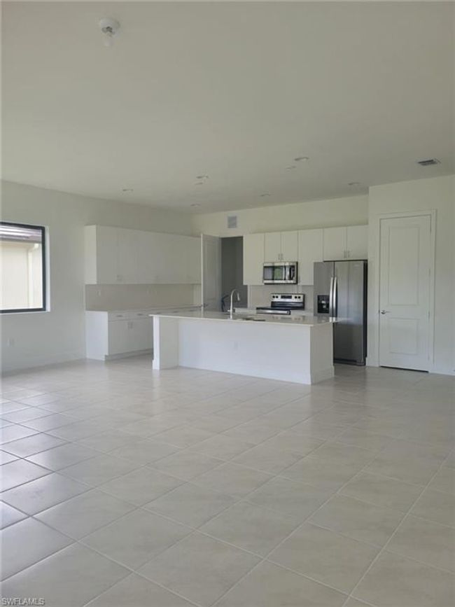 Kitchen with stainless steel appliances, light countertops, white cabinetry, light tile patterned flooring, and a kitchen island with sink | Image 5