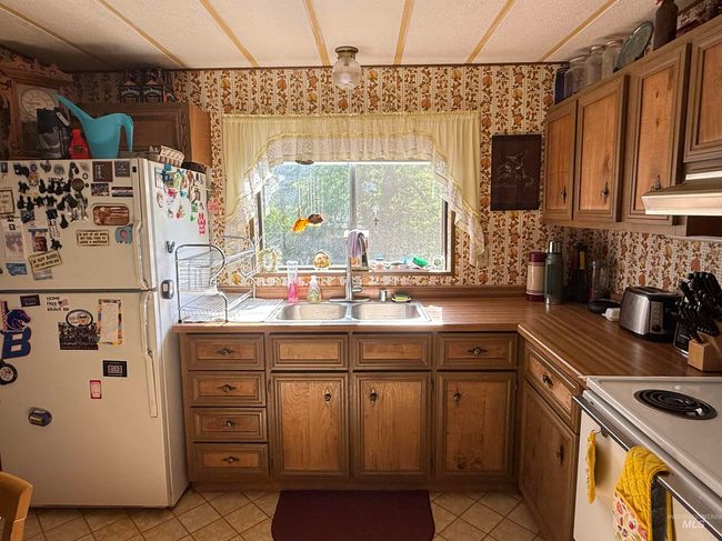 Kitchen with freestanding refrigerator, wallpapered walls, brown cabinets, light tile patterned floors, and range | Image 11