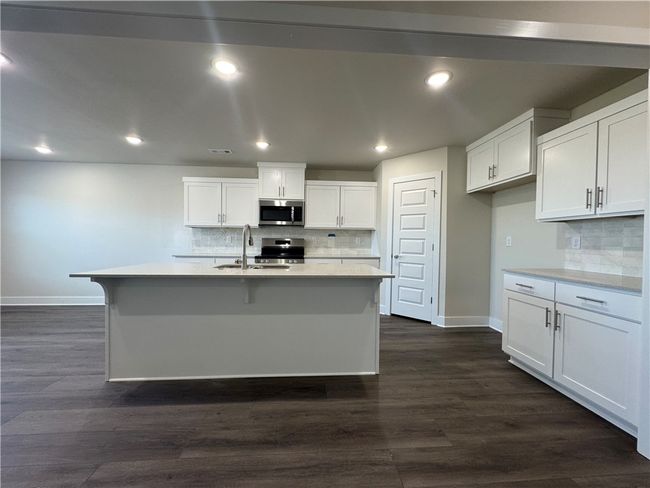 Calling all culinary enthusiasts, this home features a chef's kitchen designed to inspire with its stunning quartz countertops, expansive island providing ample prep space and seating for social gatherings, gleaming stainless steel appliances that marry form and function, and a convenient pantry to keep all your ingredients organized. | Image 6