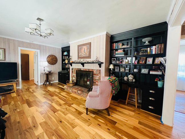 Living area with ornamental molding, a fireplace, wood finished floors, and a chandelier | Image 6