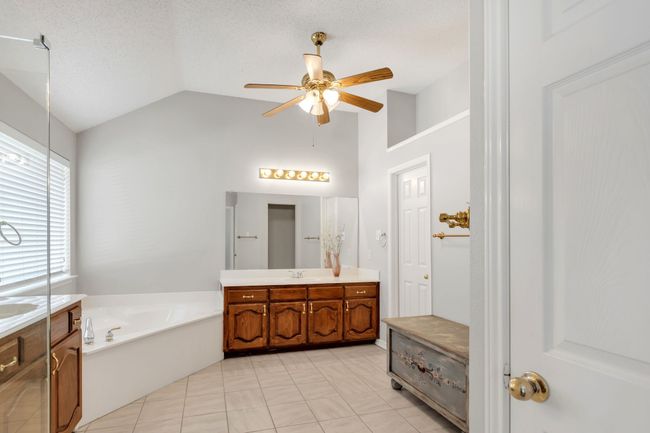 Primary bath with tile patterned floors, a ceiling fan, vanity, a garden tub, and high vaulted ceiling | Image 23