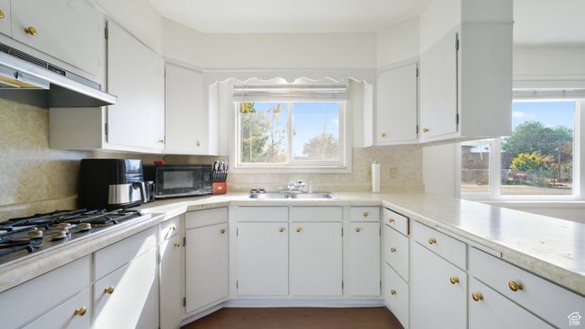 Kitchen featuring black microwave, under cabinet range hood, a sink, stainless steel gas cooktop, and backsplash | Image 5