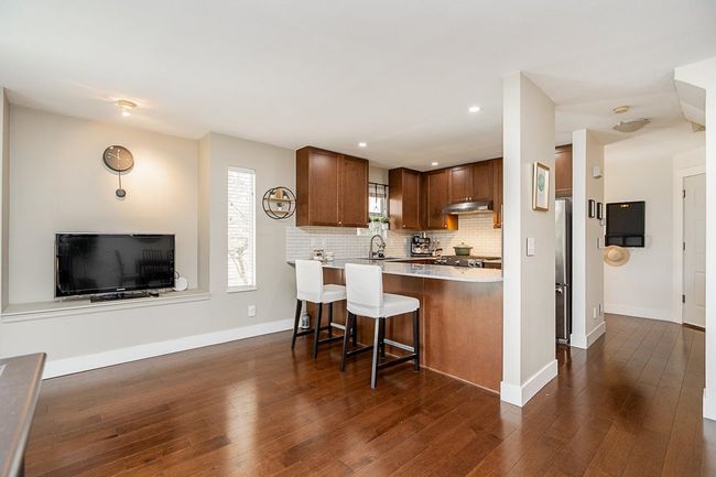 Kitchen featuring dark wood finished floors, tasteful backsplash, a peninsula, a breakfast bar, and under cabinet range hood | Image 10