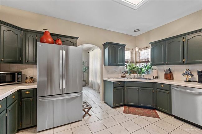 Kitchen featuring appliances with stainless steel finishes, a sink, backsplash, light tile patterned floors, and arched walkways | Image 11