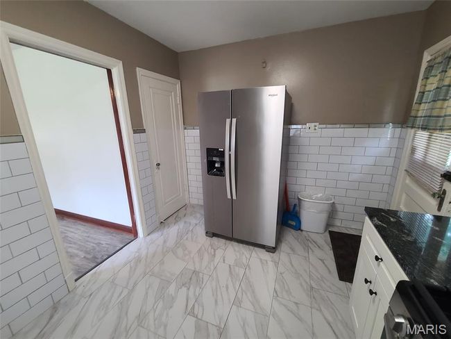 Kitchen featuring stainless steel fridge, tile walls, light marble finish flooring, white cabinetry, and dark stone countertops | Image 14