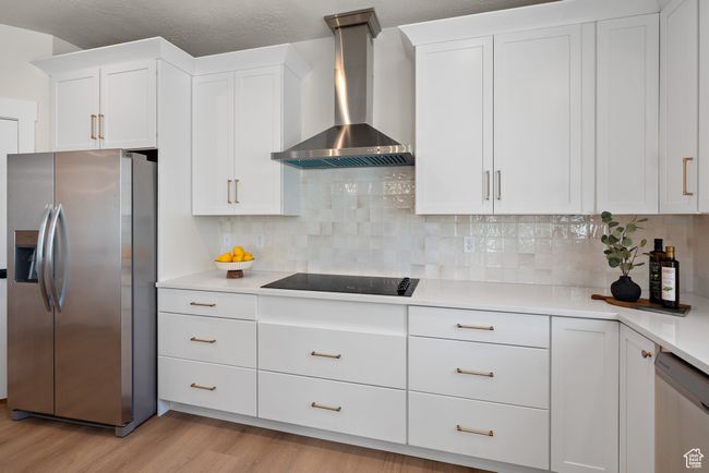 Kitchen featuring appliances with stainless steel finishes, wall chimney range hood, light wood-type flooring, light countertops, and white cabinetry | Image 13