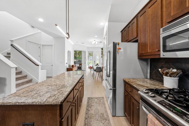 Kitchen featuring stainless steel appliances, tasteful backsplash, a kitchen island, light stone countertops, and light wood-style flooring | Image 9