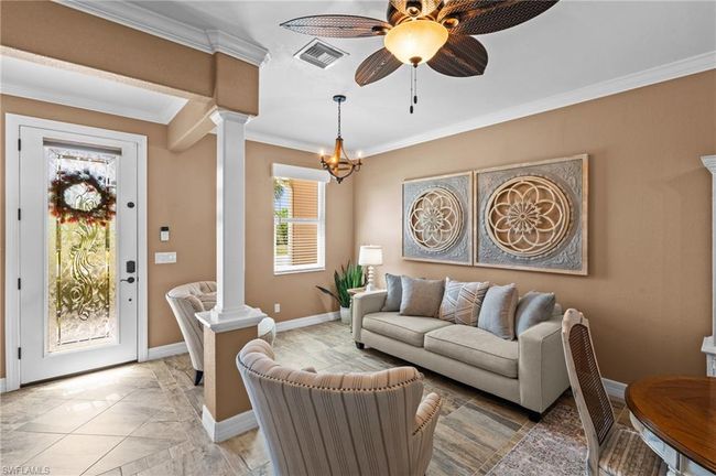 Living area with decorative columns, crown molding, baseboards, ceiling fan, and a chandelier | Image 13